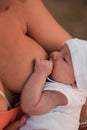 Breast feeding: Young mother breastfeeds her baby boy child outdoors wearing bright red dress - Son wears white cap - Royalty Free Stock Photo