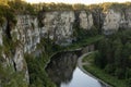 Breathtaking canyon with high rocky cliffs with thin curved river down below with reflections and lush green forest in golden.