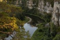 Breathtaking canyon with high rocky cliffs with thin curved river down below, reflections, lush green forest and pine