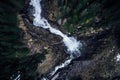 Breathtaking high angle shot of a waterfall on a rock surrounded by a forest of tall spruces