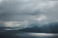 Breathtaking landscape with clouds over a lake and snowy mountains with sun rays reflected in water Royalty Free Stock Photo