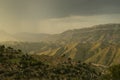 Breathtaking mountain landscape in storm weather in golden sunset with rain, ruin of medieval stone village in highlands.