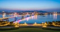 Illuminated cable-stayed bridge spanning a wide river at twilight with a city skyline in the distance Royalty Free Stock Photo