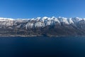 Breathtaking view of Lake Garda clear waters against a backdrop of majestic Alpine mountains, blanketed in snow during a sunny