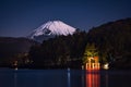 Breathtaking view of the snowy mount Fuji behind the illuminated tori gate at the Ashi lake shore