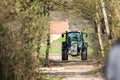 Brecht, Belgium - March 24 2019: A farmer driving a green Fendt tractor through a forest on a farm path. Both sides of the road