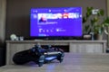 BRECHT, BELGIUM Ã¢â¬â MARCH 28 2019: A wide portrait of a Sony Playstation 4 controller on a wooden table in front of a telivision