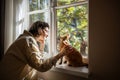 Tender pet lover stroking beloved adorable breed cat Devon Rex sitting on windowsill in sunlight