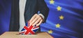 Brexit Voting concept. Man putting a ballot with British Flag into a voting box with European Union flag on background