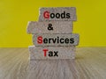 Brick blocks with words Goods and services tax on yellow background. Beautiful wooden table. State financial policy to regulate