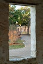 Brick building window with no glass or frame and tree and sidewalk outside view from dark interior in afternoon shade