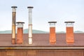 Brick chimneys and tin ventilation pipes on the roof of a wooden hut on a background of green hills on a cloudy day Royalty Free Stock Photo