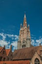 Brick church steeple, roofs and public lamp contrasting with blue sky in Bruges.