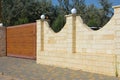 A brick fence with lanterns and wooden sliding gate in the paver block street