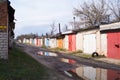 Brick garages with bright metal doors in the city on a spring day with puddles on the road after rain.