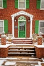 Brick house with bright green trim and shutters in snow -closeup of entrance with rock steps