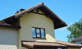 A brick house with a clay roof edging with gable rakes, chimney, ventilation, wooden fascia board, soffit, roof gutters, and attic