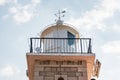 The stone brick and metal dome of the lighthouse with the directions of the world. White arrows in a cloudy sky designating north