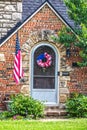 Brick and rock cottage with arched front door surrounded by strones with mounted American flag and red white and blue wreath on Royalty Free Stock Photo