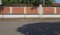 Brick wall with columns and lower side made of bricks. Porphyry sidewalk, yellow pole and asphalt street in front.