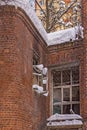 Brick wall of an old abandoned house with broken glasses in the windows and with snow drifts on the background of a new house. Royalty Free Stock Photo