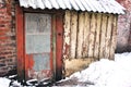 Brick wall of residential building with wooden door with red shabby paint and slate roof with snow Royalty Free Stock Photo