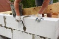 Bricklayer builder laying autoclaved aerated concrete blocks for house wall near unfinished roof wooden beams Royalty Free Stock Photo