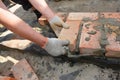 Bricklayer hands laying the first course of bricks on house foundation wall with bitumen waterproof barrier Royalty Free Stock Photo