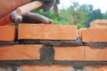 Bricklayer lays bricks on cement mortar. Builder hold brick with hand and knocks with a hammer from above during house wall Royalty Free Stock Photo