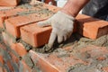 The bricklayer, mason craftperson in protective gloves is laying red bricks in cement mortar to construct a wall of a house