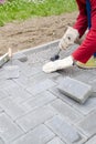 Bricklayer places concrete paving stone blocks for building up a patio, using hammer and spirit level