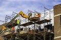 A bricklayer on scaffolding directs the delivery of bricks from a telescopic forklift during building construction