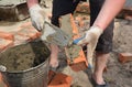 Brickwork and bricklaying: a workman is applying mortar, cement on a brick with a trowel to build a brick wall of a house on a