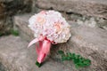 Bridal bouquet of pink roses and hydrangea, with pink ribbons down on the stone steps and wedding rings near it Royalty Free Stock Photo