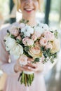 Bridal bouquet from pink roses and white tupils in young bride hands, focus of flowers. Spring freshness of tulips and roses in o