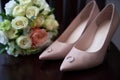 Bridal bouquet of roses and greenery with satin ribbon, pink women shoes and two golden wedding rings on wood table. Royalty Free Stock Photo