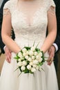 Bridal bouquet on the wedding day. Beautiful girl holding a bouquet of white tulips. The groom hugs the waist of the bride. Royalty Free Stock Photo