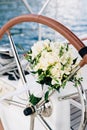 Bridal bouquet of white peonies, freesia, boxwood branches and white ribbons on the sailboat wheel