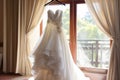 Bridal elegance Wedding dress hangs on a curtain rail near window Royalty Free Stock Photo