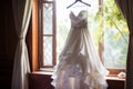 Bridal elegance Wedding dress hangs on a curtain rail near window Royalty Free Stock Photo