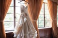 Bridal elegance Wedding dress hangs on a curtain rail near window