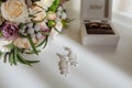 Bridal morning details composition. Top view of wedding rings, beautiful bouquet of flowers with ribbons, earrings. Flat Royalty Free Stock Photo