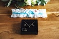 Bride accessories: black jewelry box with golden ring, necklace and earrings on wooden board. White lace garter with