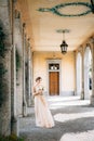 Bride in a beautiful dress with a bouquet of pink flowers stands in an arched hall. Lake Como, Italy