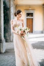 Bride in a beautiful dress with a bouquet of pink flowers stands in the vaulted hall with her head turned. Lake Como