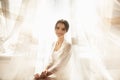 Bride in beautiful dress sitting on chair indoors in white studio interior like at home. Trendy wedding style shot