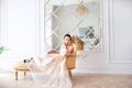 Bride in beautiful dress sitting on sofa indoors in white studio interior like at home. Trendy wedding style .