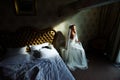 Beautiful redhair lady in elegant white wedding dress. Fashion portrait of model indoors. Beauty woman sitting near her bed Royalty Free Stock Photo