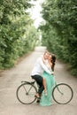 Bride and groom sit on bicycle on forest road, embrace and kiss.