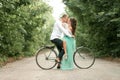Bride and groom sit on bicycle on forest road, embrace, laugh an